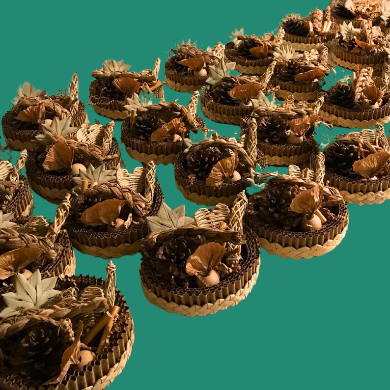 May include: A group of small, handmade baskets. Each basket is made from corrugated cardboard and filled with natural items such as pine cones, dried leaves, and small, round objects. The baskets have woven handles and are set against a teal background.