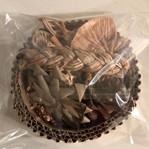 May include: A circular bird toy made from natural, woven plant fibres, presented in a clear plastic bag. It is set within a corrugated cardboard base. The colours are predominantly tan and brown.