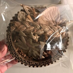 May include: A round, woven basket filled with dried leaves and twigs. The basket is made of natural fibres and is encased in clear plastic. The rim of the basket is made of corrugated cardboard.
