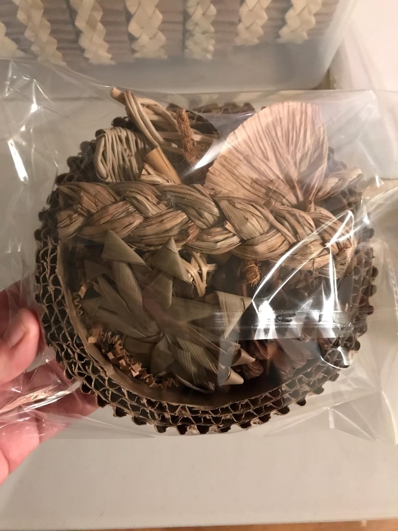 May include: A round, woven basket filled with dried leaves and twigs. The basket is made of natural fibres and is encased in clear plastic. The rim of the basket is made of corrugated cardboard.