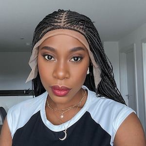 May include: A woman with black braided hair wearing a black and white shirt with a gold necklace. The necklace has a crescent moon pendant and a star pendant.