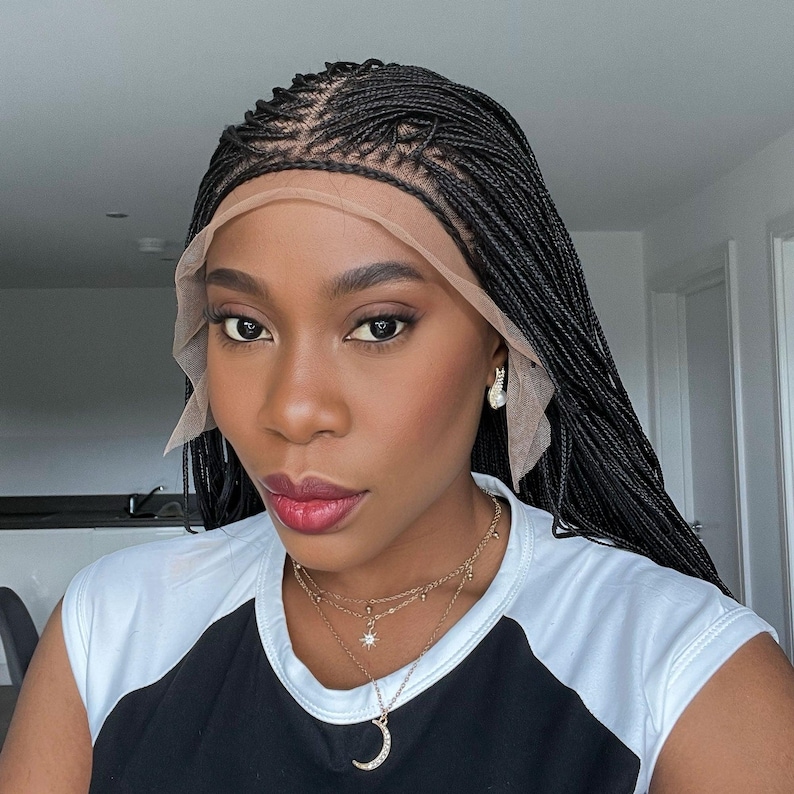 May include: A woman with black micro braids styled into a wig. The wig is worn with a nude lace front cap. She is wearing a black and white striped shirt and a gold necklace with a crescent moon pendant.