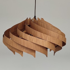 Puede incluir: Una lámpara colgante de madera con un diseño único y en capas. La lámpara está hecha de múltiples tiras finas de madera que están curvadas y superpuestas para crear una forma espiral. La lámpara está suspendida del techo por un delgado cable negro.