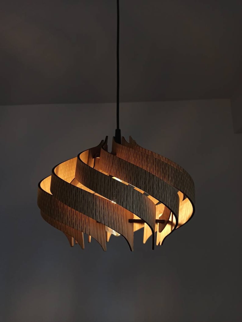 May include: A wooden pendant light fitting with a unique, swirling design. The light is made of multiple layers of wood, creating a layered effect. The light is on and casting a warm glow.