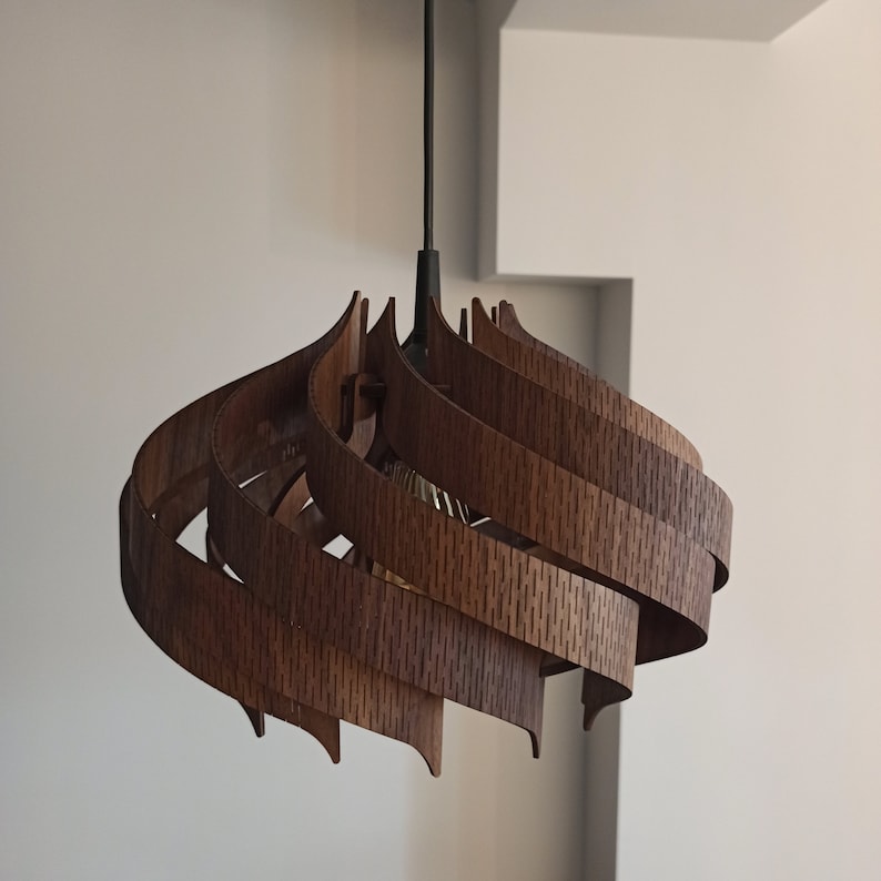 May include: A wooden pendant light fixture with a unique, swirling design. The light is made of multiple layers of wood, creating a modern and organic look.
