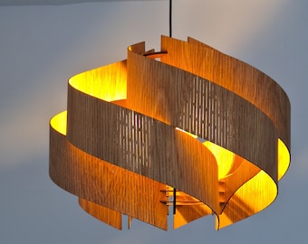 Può includere: Una lampada a sospensione in legno moderna con un design unico e stratificato. La luce è realizzata con sottili strisce di legno curve che sono impilate l'una sull'altra per creare una forma a spirale. La luce è illuminata dall'interno, proiettando un bagliore caldo.