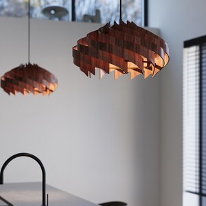 May include: Two wooden pendant lights with a spiral design hang from the ceiling. The lamps are made of dark brown wood and emit a warm, inviting glow. The lights are suspended above a kitchen island.