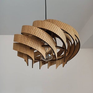 May include: A wooden pendant light fitting with a unique, geometric design. The light fitting is made of multiple layers of wood that are stacked and curved to create a spiral shape. The light fitting is suspended from the ceiling by a black cord.