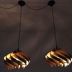 May include: Two wooden pendant lights with a swirling design hang from the ceiling. The lights are turned on and emit a warm glow.