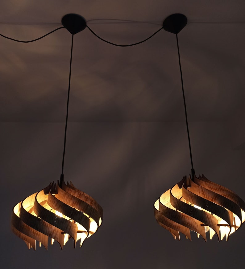 May include: Two wooden pendant lights with a swirling design hang from the ceiling. The lights are turned on and emit a warm glow.