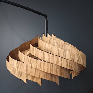 Może przedstawiać: Nowoczesna drewniana lampa wisząca o spiralnym, warstwowym wzorze. Lampa jest zawieszona na czarnym metalowym ramieniu.