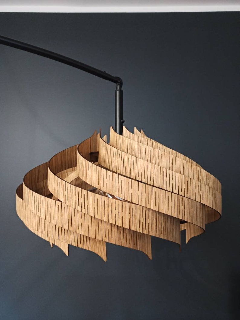 Może przedstawiać: Nowoczesna drewniana lampa wisząca o spiralnym, warstwowym wzorze. Lampa jest zawieszona na czarnym metalowym ramieniu.