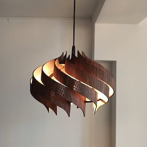 May include: A modern, wooden pendant light fixture with a unique, swirling design. The light is made of multiple layers of wood, creating a warm and inviting ambiance.