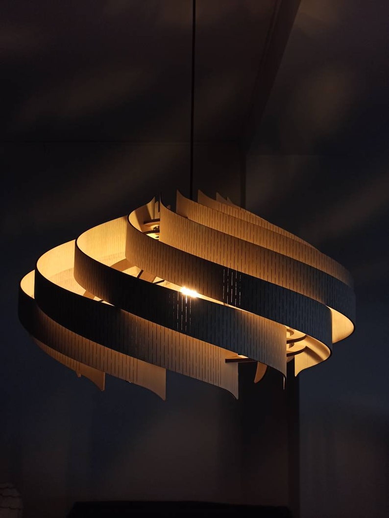 May include: A modern, wooden pendant light fixture with a swirling, layered design. The light is turned on and emits a warm glow.