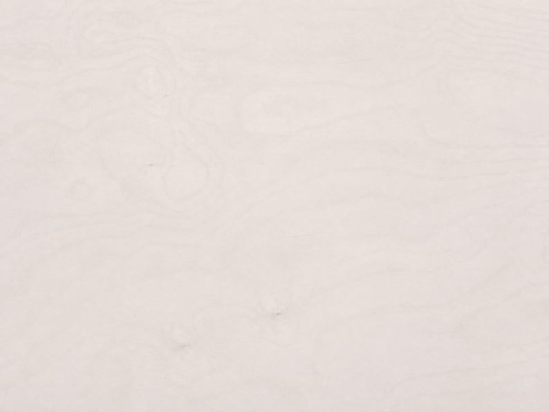 May include: A light off-white wooden surface featuring a subtle, natural grain pattern with soft, flowing lines and organic swirls. The texture is smooth and uniform, displaying a pale, neutral color palette throughout the entire visible area.