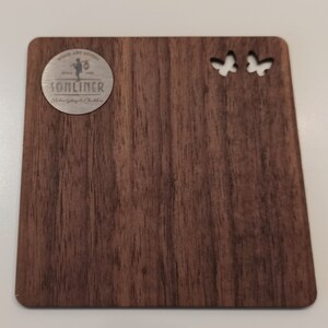 May include: A wooden plaque with a dark brown woodgrain finish. The plaque has two butterfly cutouts in the top right corner. A circular metal emblem with the text "SONLINER" is in the top left corner.