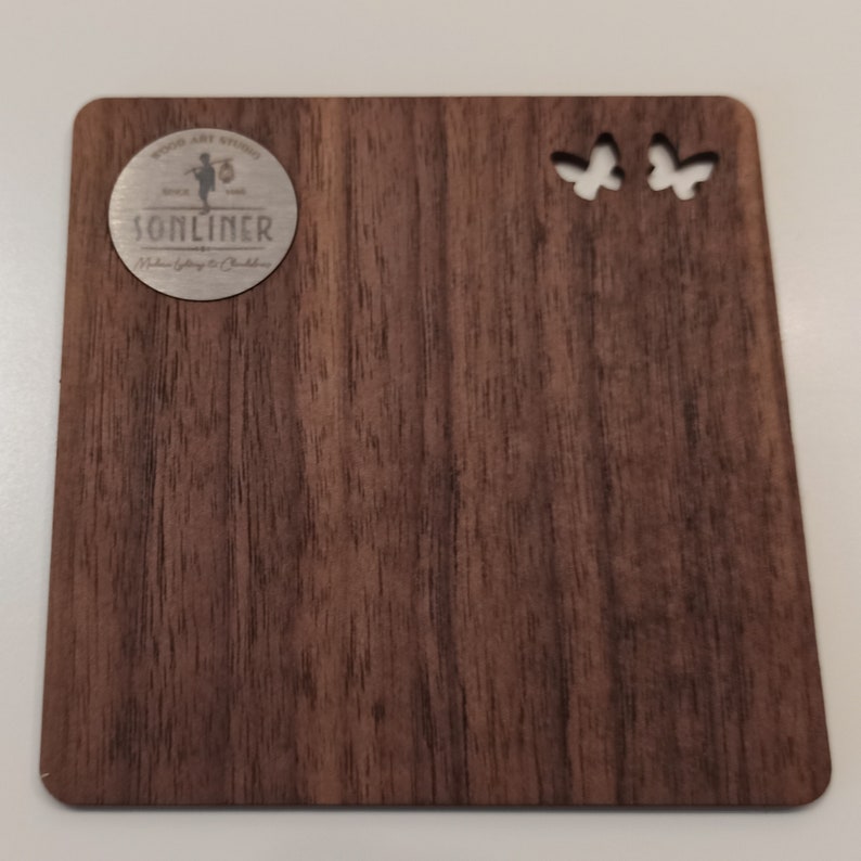 May include: A wooden plaque with a dark brown woodgrain finish. The plaque has two butterfly cutouts in the top right corner. A circular metal emblem with the text "SONLINER" is in the top left corner.