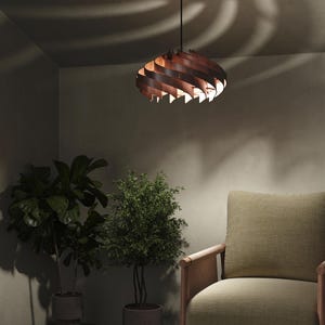May include: A wooden pendant light fixture with a spiral design hangs from the ceiling. The light fixture is brown and casts a warm glow. The room also features a green armchair, potted plants, and a neutral-toned wall.