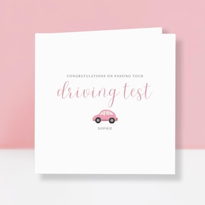 May include: A white card with the message "Congratulations on passing your driving test" in pink script. A pink car illustration is below the text, with the name "Sophie" beneath it. The card is set against a pink backdrop.