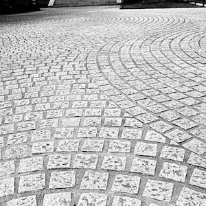 May include: A black and white photo of a cobblestone walkway with a curved pattern.