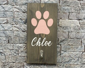 May include: A wooden sign with a pink paw print and the name "Chloe" written in white. The sign has a metal hook on the bottom.