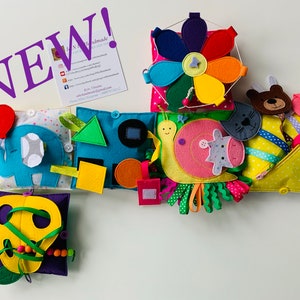 Può includere: Un set di giocattoli di attività in feltro colorati per neonati e bambini piccoli. Il set include un mobile a forma di fiore, una lumaca con una mucca e un gatto, una tasca gialla con un orso e un maiale, un quadrato blu con forme, un quadrato bianco con un elefante e un palloncino, e un quadrato viola con una foglia gialla e perline.