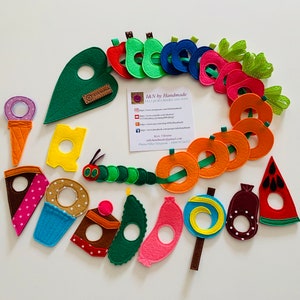 Puede incluir: Un juego de fieltro con la historia de La Oruga Muy Hambrienta. El juego incluye una oruga verde, una manzana roja, una pera verde, una ciruela azul, una naranja naranja, un limón amarillo, una fresa rosa, un cono de helado morado, un trozo de queso amarillo, un pastel de chocolate marrón, un cupcake azul, un pepinillo verde, un plátano rosa, una piruleta azul, un trozo de chocolate marrón y una sandía roja.