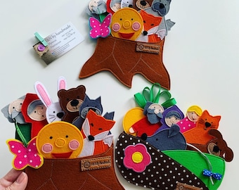 Puede incluir: Marionetas de dedos de fieltro en un tocón de árbol de fieltro marrón. Las marionetas incluyen una caperucita roja, un lobo, un conejito, un oso, un zorro y una niña. Las marionetas están dispuestas en círculo alrededor de un sol de fieltro amarillo con una cara sonriente. El tocón de árbol tiene una base de fieltro marrón y una parte superior de fieltro verde. Las marionetas están todas hechas a mano y son perfectas para el juego imaginativo.