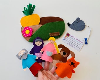 Puede incluir: Marionetas de dedo de fieltro de una niña, un niño, un perro, un gato y un ratón. Las marionetas están en una mano con un fondo de fieltro verde y marrón. El fondo también tiene una piña de fieltro amarilla y una flor de fieltro rosa. El texto en la tarjeta dice "I&N by Handmade Felt & Craft Toys".