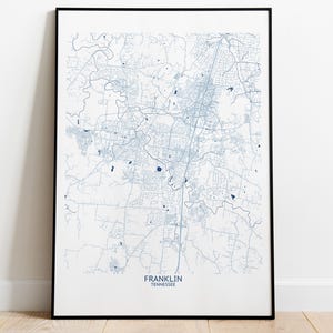 May include: Framed map print of Franklin, Tennessee, in a minimalist style. The map features a detailed blue outline of the city's streets and waterways against a white background. The city name and state are printed at the bottom.