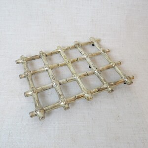 May include: A silver-toned metal hot pad with a woven bamboo design. The hot pad is rectangular and has a grid pattern.