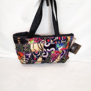 May include: A small, patchwork tote bag with black straps. The bag is made of different fabrics in various colors, including purple, red, green, and gold. The bag has a label that says "Lilith" with a website address.