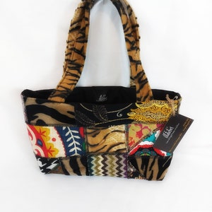 May include: A small patchwork tote bag with tiger print fabric and colourful geometric patterns. The bag has black fabric lining and two handles. The bag has a tag that says "illdeart".