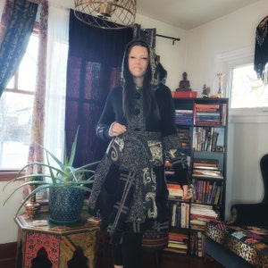 May include: A black and white hooded jacket with a patchwork design. The jacket features a hood with a drawstring and a button closure. The jacket is layered with different fabrics and textures, including a black and white plaid, a black and white floral print, and a black and white geometric pattern.