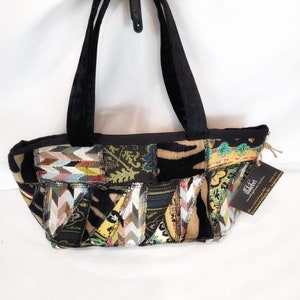 Könnte beinhalten: Eine schwarze Patchwork-Tragetasche mit einem schwarzen Samtband. Die Tasche ist aus verschiedenen Stoffen mit einer Vielzahl von Mustern und Farben gefertigt, darunter Braun, Grün, Gelb und Blau. Die Tasche hat ein kleines Etikett, das an ihr befestigt ist und "lifeboat" sagt.