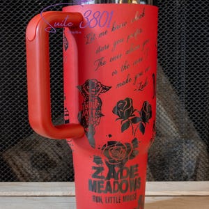 May include: Red stainless steel tumbler with a black handle and a black design featuring roses, a butterfly, and the text "Let me know which stars you prefer. The ones above you or the ones I make you see." -Zade. The tumbler also features the text "Zade Meadows" and "Run, Little Mouse".