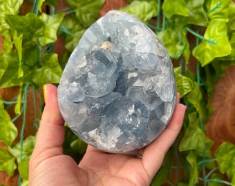 May include: A light blue celestite crystal cluster with a rough, natural surface. The crystal is a heart shape and has a white, cloudy appearance.