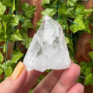 May include: A clear quartz crystal point with a unique, faceted shape. The crystal is clear and has a slight sparkle. It is a natural crystal and has a rough, unpolished texture.