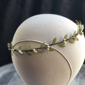 May include: A delicate floral crown with white flowers and green leaves. The crown is made of wire and is designed to be worn on the head.