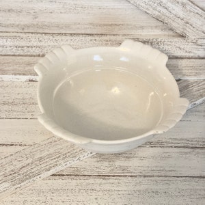 May include: A white ceramic bowl with a scalloped rim. The bowl is sitting on a whitewashed wood surface.