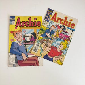 Può includere: Due fumetti vintage di Archie. Uno ha una copertina gialla con Archie in un maglione blu e la parola "Archie" in rosso. L'altro ha una copertina bianca con Archie e amici che lavano un'auto, con la parola "Archie" in rosso.