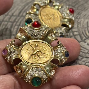 Pendientes de clip vintage estilo etrusco Gripoix en tono dorado con un ángel cargando a otro ser. Grandes pendientes de clip con piedras artificiales de colores.