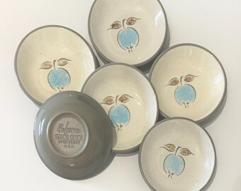 May include: A set of six vintage stoneware bowls. The bowls have a cream-colored interior with a blue apple design and brown leaves. The rims are gray. One bowl is upside down, revealing a gray base with text.