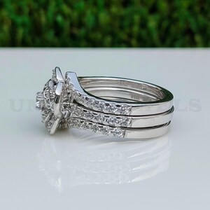 May include: A three-piece silver ring set. The engagement ring features a central cluster of small, round stones. Two additional bands are encrusted with smaller stones. The rings are displayed on a white surface with a blurred green background.