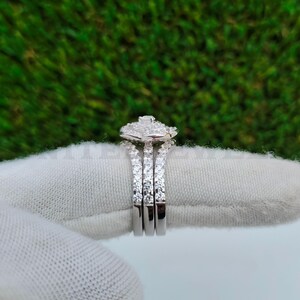 May include: A three-piece diamond ring set. The rings are silver-colored with multiple small diamonds set in the bands. The top ring has a square cluster of diamonds. The background is a green, textured surface.