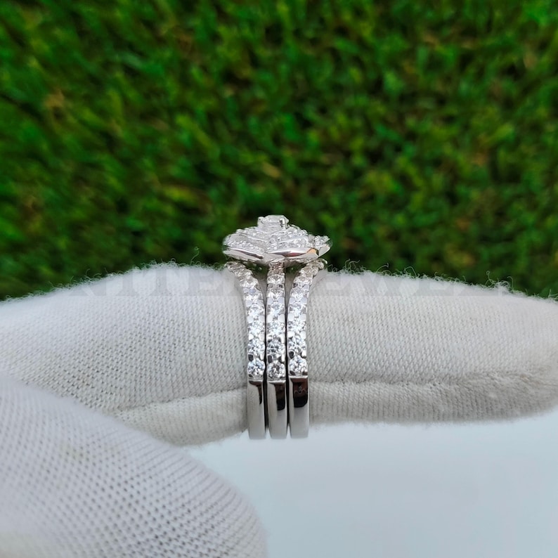 May include: A three-piece diamond ring set. The rings are silver-colored with multiple small diamonds set in the bands. The top ring has a square cluster of diamonds. The background is a green, textured surface.