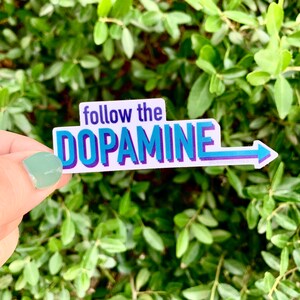 Pu&ograve; includere: Etichetta bianca con testo blu e viola che dice "follow the DOPAMINE" con una freccia blu che punta a destra.