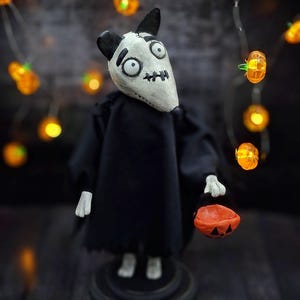 Handmade Sparky Art Doll wearing a black hoodie Halloween-style outfit, holding a pumpkin-shaped trick-or-treat box. Standing straight, facing slightly to the right. Whimsical and spooky Halloween home decor, unique collectible dog doll