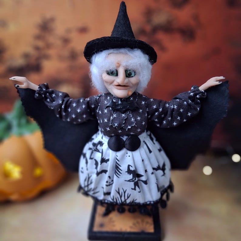 Front view of the handmade witch art doll wearing a witch-themed Halloween outfit with bat wings fully spread, standing upright as a spooky seasonal decor piece.