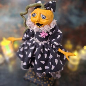 Close-up left side view of the handmade spooky Halloween pumpkin art doll, highlighting her hand-painted face, pumpkin-inspired outfit, and festive Halloween accents.